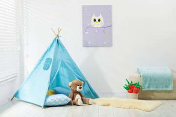 Wigwam, toys, pouf and pillows near white wall in child's room © New Africa