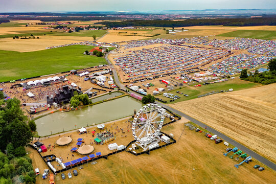 Herzogenaurach, Germany - 22 July 2022: Aerial view of the Open Beatz Festival featuring a Ferris wheel, large stages, and a massive parking area surrounded by rural fields.