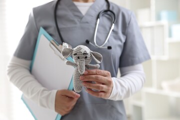 Pediatrician holding toy elephant with adhesive bandages and clipboard in clinic, closeup