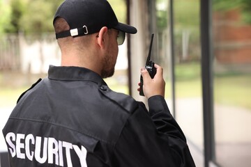 Obraz premium Security guard in uniform using walkie talkie outdoors, space for text