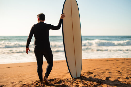 Surfer in wetsuit carrying surfboard walking to ocean
