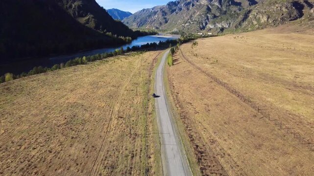 Aerial Road Through Valley With Car, Golden Meadow, Distant Lake And Craggy Mountains Solo Driver On Reflective Road Trip, Landscape Photographer Framing Shots, Nature Observer Pausing At Overlook