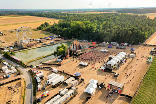 Herzogenaurach, Germany - 22 July 2022: Aerial view of the Open Beatz Festival featuring a large stage, a Ferris wheel, and crowds of people surrounded by forests and wind turbines.