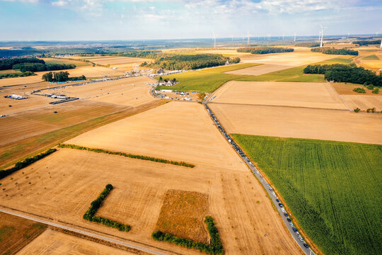 Herzogenaurach, Germany - 22 July 2022: Aerial view of the Open Beatz Festival site surrounded by golden fields, wind turbines, and a long line of cars on a sunny day.
