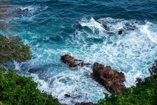 Powerful turquoise sea waves crashing against wild coastal rocks, view from Marimurtra Botanical Garden, Blanes, Costa Brava. Dynamic Mediterranean seascape, blue mind wellness and wild nature travel 