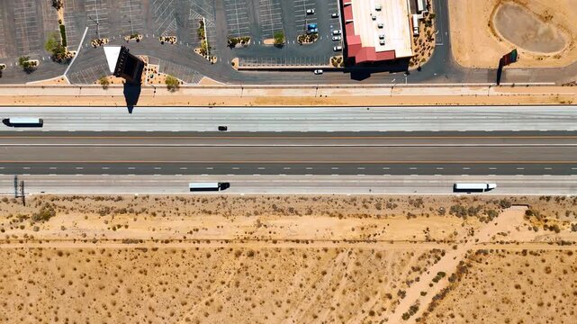 Rising over the multi-lane motorway crossing the deserted landscape. A large parking lot with few cars is along the highway.