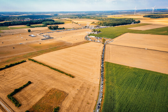 Herzogenaurach, Germany - 22 July 2022: Aerial view of the Open Beatz Festival site with a long queue of cars on a rural road surrounded by golden fields and wind turbines.