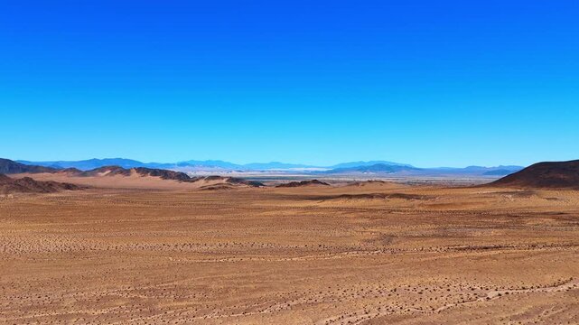 Flight over the plain valley in the dry desert. Approaching the rocks in the arid area of California, USA on sunny clear day.