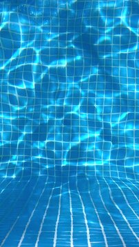 Clear blue swimming pool water with sunlight reflections over tiled walls and floor. Abstract summer background for spa, resort and relaxation concepts.