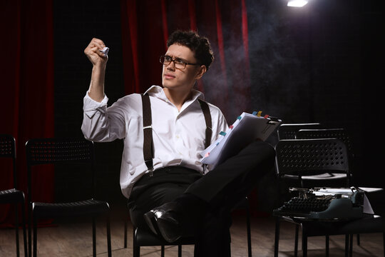 Stressed male screenwriter with scenario and crumpled paper sitting in chair on scene