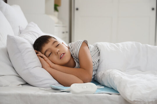 Little boy sleeping under blanket on electric heating pad in bedroom
