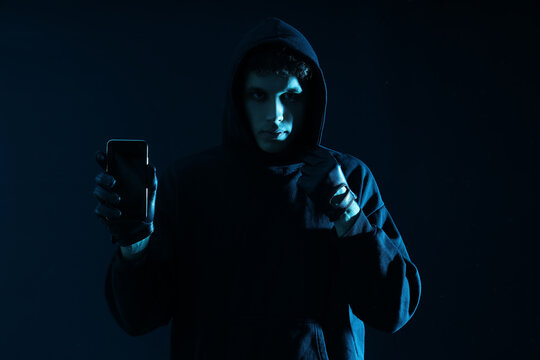 Male fraudster with mobile phone on dark background