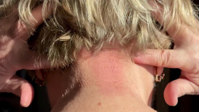 Close-up occipital self massage on white woman, fingers pressing and sliding back and forth at base of skull, short gray hair