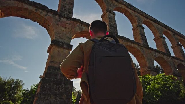 Traveler with backpack exploring Les Ferreres Aqueduct known as Pont del Diable near Tarragona Spain at sunset