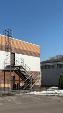 Modern building exterior with iron staircase, siding covered roof and metal ladder cage. Brown cladding over white wall