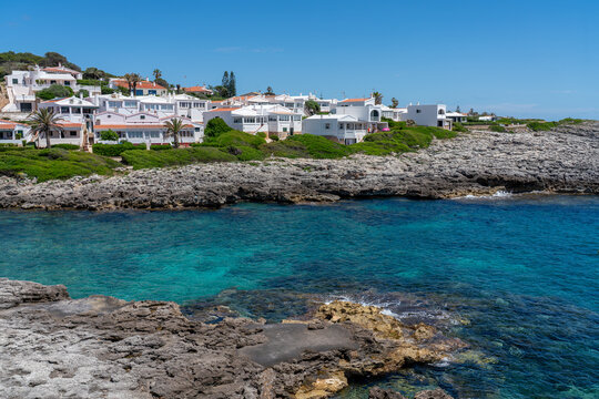 Scenic view of Binibeca Vell whitewashed village on the rocky coast of Menorca, Spain. Luxury Mediterranean real estate, turquoise sea bay, and summer holiday travel concept.