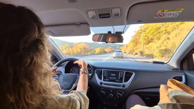 Driving road trip travel view from inside the car as a young woman steers through autumn mountain foliage on a sunny highway journey.