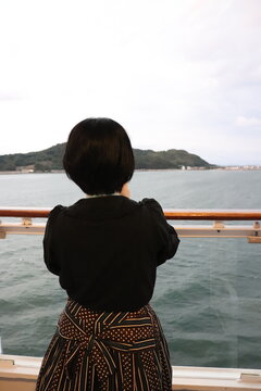 クルーズ船から海上の島を見る女性の後ろ姿