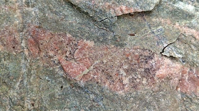 Horizontal close-up of rough geological rock surface showing a pink mineral vein with prominent cracks and fissures. Abstract macro backdrop of layered natural stone, detailed organic rock pattern