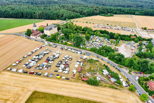 Eggolsheim, Germany - 09 May 2026: Aerial view of Schloss Jagersburg with a crowded parking lot of campers and cars surrounded by agricultural fields and lush green forests.