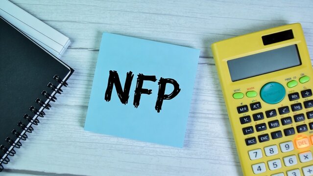 A close-up view of a yellow calculator, black notebook, and blue sticky note with NFP written on it, lying on a white wooden desk.