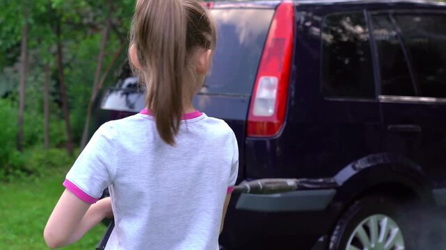 Little girl washes car with pressure washer outdoors in nature. Child washes car headlight. High pressure car wash
