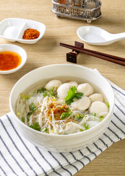 Clear noodle soup with pork meatballs in a white bowl on a wooden table.