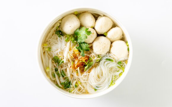 Clear noodle soup with pork meatballs in a white bowl on a white background.