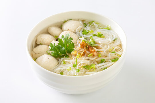 Clear noodle soup with pork meatballs in a white bowl on a white background.