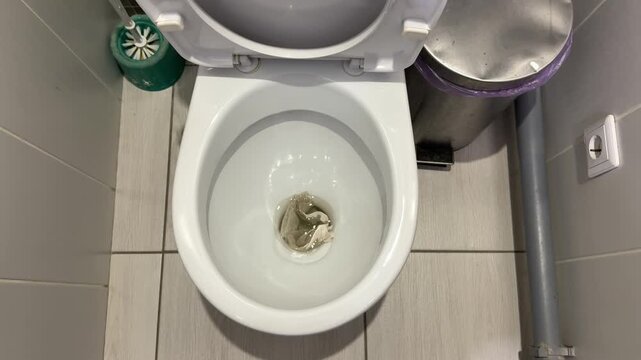 White porcelain toilet bowl stained with urine, overhead view in tiled bathroom showing toilet brush, gray plumbing pipe, used