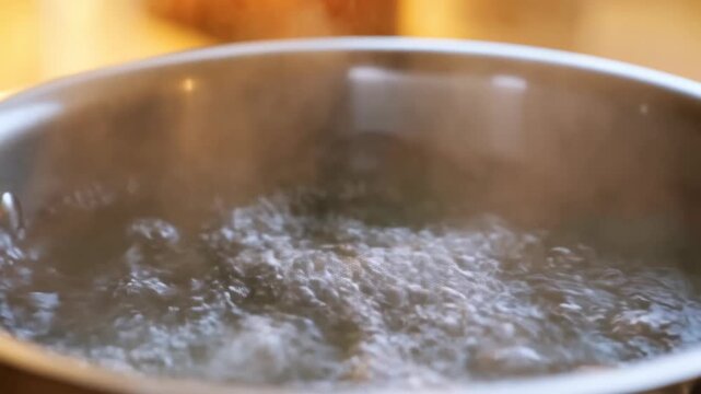 Static close-up shot of water vigorously boiling in metal pot on stove with steam and bubbles