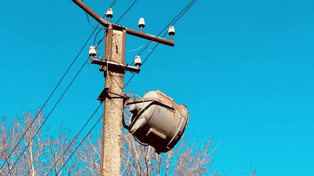 Spotlight on concrete pole, blue sky. Side view of large industrial light fixture hanging from utility pole, power wires crossing