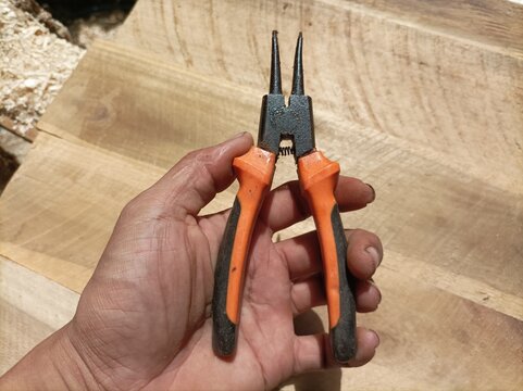 Hand holding small orange black circlip pliers on wooden surface.