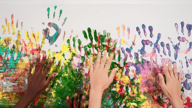 Diverse student hand placed on colorful stained wall while switch place. Closeup of hand or children with mixed races paint their hand print and moving. Background. Creative activity. Edification