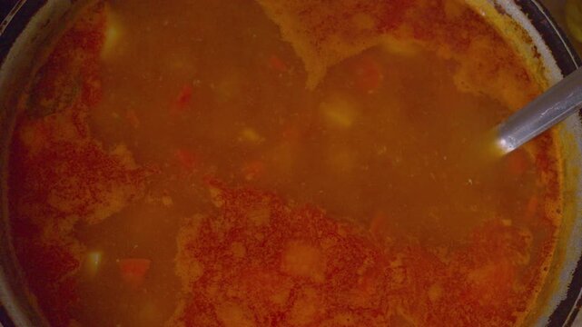The process of preparing a home-cooked meal. A rich meat and potato soup simmers in a rustic cast-iron pot. Bubbles burst on the surface of the hot broth, steaming.
