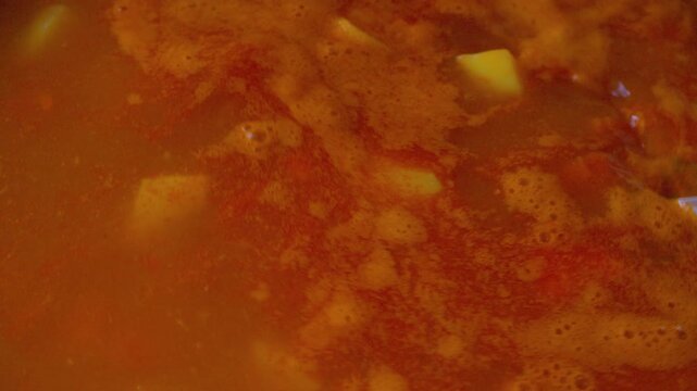 A close-up shot from above, showing simmering hot meat and potato soup simmering in a cast-iron pot. The broth simmers, billowing steam, and the delicious gourmet dish. The process of home cooking.