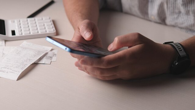 Hands Holding Phone Over Receipts, Calculator Nearby, Freelancer Reviewing Expenses For Side Hustle, Soft Warm Lighting, Neutral Desk Background, Closeup Focused Workflow