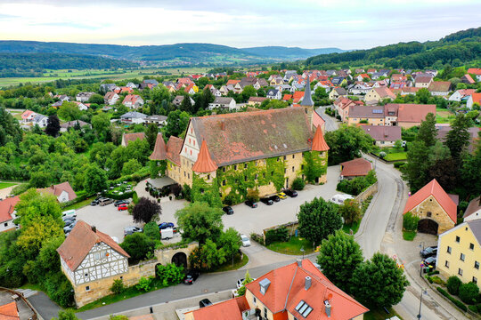 Wiesenthau, Germany - 09 May 2026: Aerial view of Schloss Wiesenthau with its ivy-covered walls and red-tiled roofs, surrounded by traditional village houses and lush green hills.