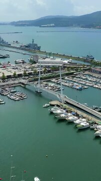 Vertical video. La Spezia, Italy. Ponte Thaon di Revel, a sleek white cable-stayed pedestrian bridge spanning the harbor, Drone footage over Porto Mirabello marina and naval vessels. Drone footage, P