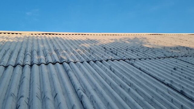 Corrugated asbestos roof with a clear blue sky background and tree shadows during daytime