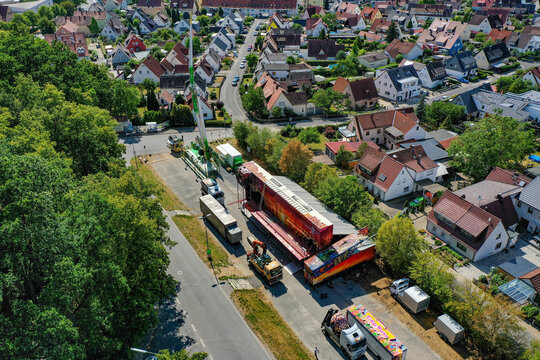 Forchheim, Germany - 27 July 2023: Aerial view of the setup for the Annafest festival with large trucks and fairground trailers parked near a residential neighborhood and lush trees.