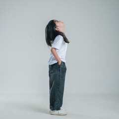Side profile portrait of young Asian girl looking upward while standing casually with hands in pockets isolated on white studio background. © Rangga Ispraditya