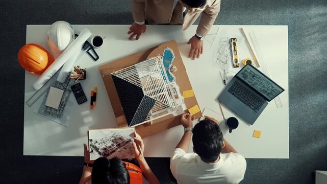 Top aerial view of architect engineer team stick sticky notes on house model while working together to design building construction at table with laptop, safety helmet and project plan. Alimentation.