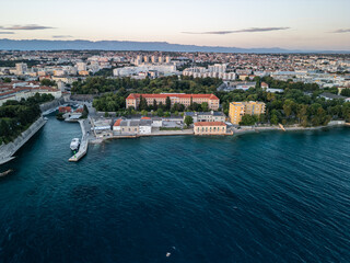 Fototapeta premium Croatia - 05 17 2025: Angled drone photo showing Vladmir Nazor’s Grammar School, nearby lower buildings with solar panels, Molo Terraferma Marina, Adriatic Sea with boats and seagulls, Zadar beach