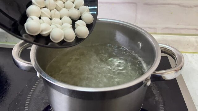 Boiling water in a stainless steel pot on a stove, with small round dumplings being added, leading to the dumplings floating in the bubbling water, illustrating the cooking process
