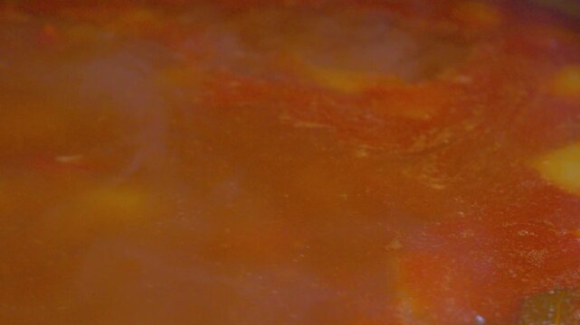 The process of preparing a home-cooked meal. A rich meat and potato soup simmers in a rustic cast-iron pot. Bubbles burst on the surface of the hot broth, steaming.
