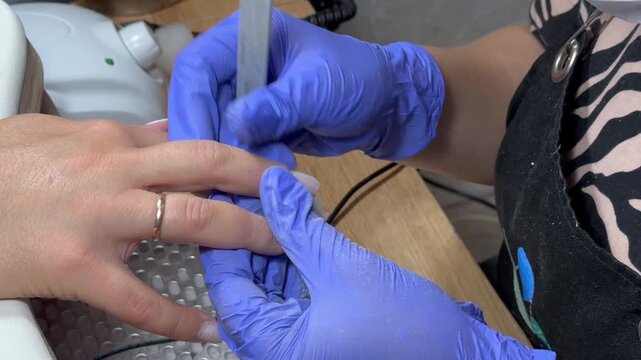 Video of a nail technician filing nails. Manicurist shapes nail using salon nail file during cosmetic procedure in beauty salon. Woman gets a french manicure at a beauty salon, manicurist files her cu