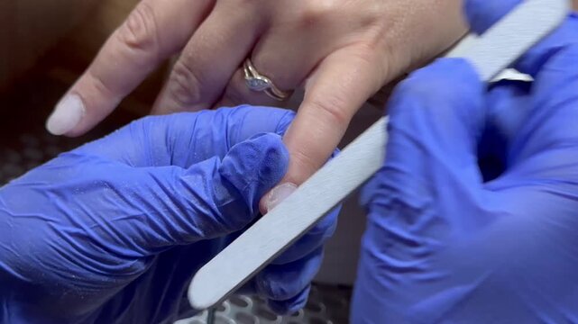 Video of a nail technician filing nails. Manicurist shapes nail using salon nail file during cosmetic procedure in beauty salon. Woman gets a french manicure at a beauty salon, manicurist files her cu