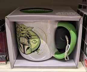 Naklejka premium Taza oficial de la serie The Mandalorian de Star Wars, con el dibujo de Grogu y del casco del Mandalorian, en estante de juguetería Toy Planet en Madrid, España, 7 de abril de 2026