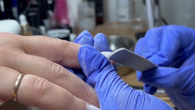 Video of a nail technician filing nails. Manicurist shapes nail using salon nail file during cosmetic procedure in beauty salon. Woman gets a french manicure at a beauty salon, manicurist files her cu